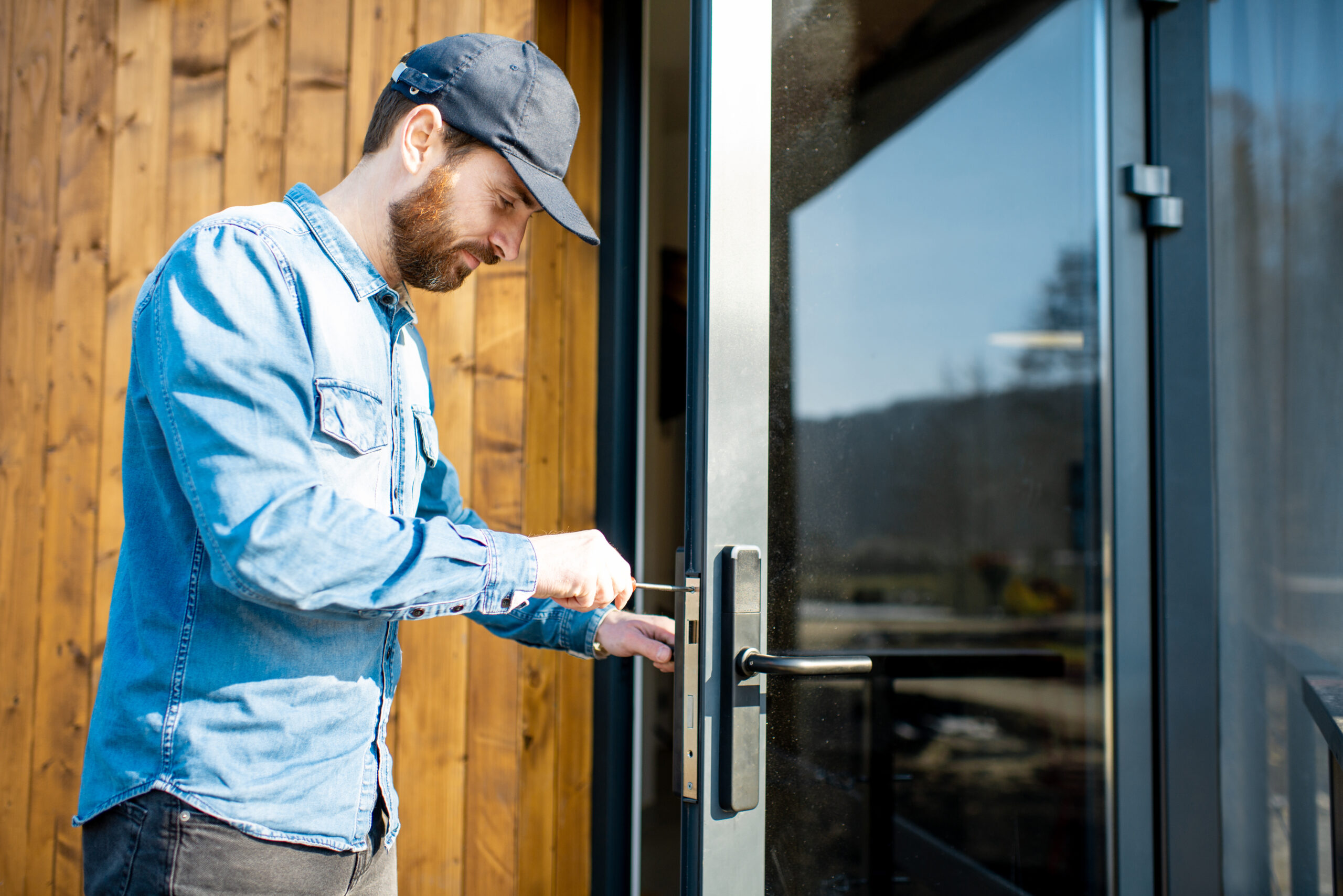 Workman repairing entrance door lock of the modern house or hotel during the sunny weather outdoors